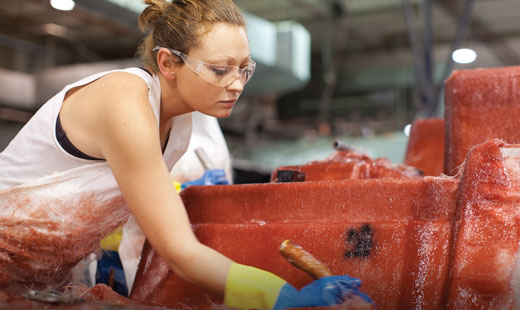 A factory employee rolls fiberglass on a MasterCraft boat